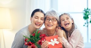 Alt="Happy mother's day! Child and mom congratulating granny giving her flowers tulips ang gift box. Grandma, mum and girl smiling and hugging. Family holiday and togetherness."