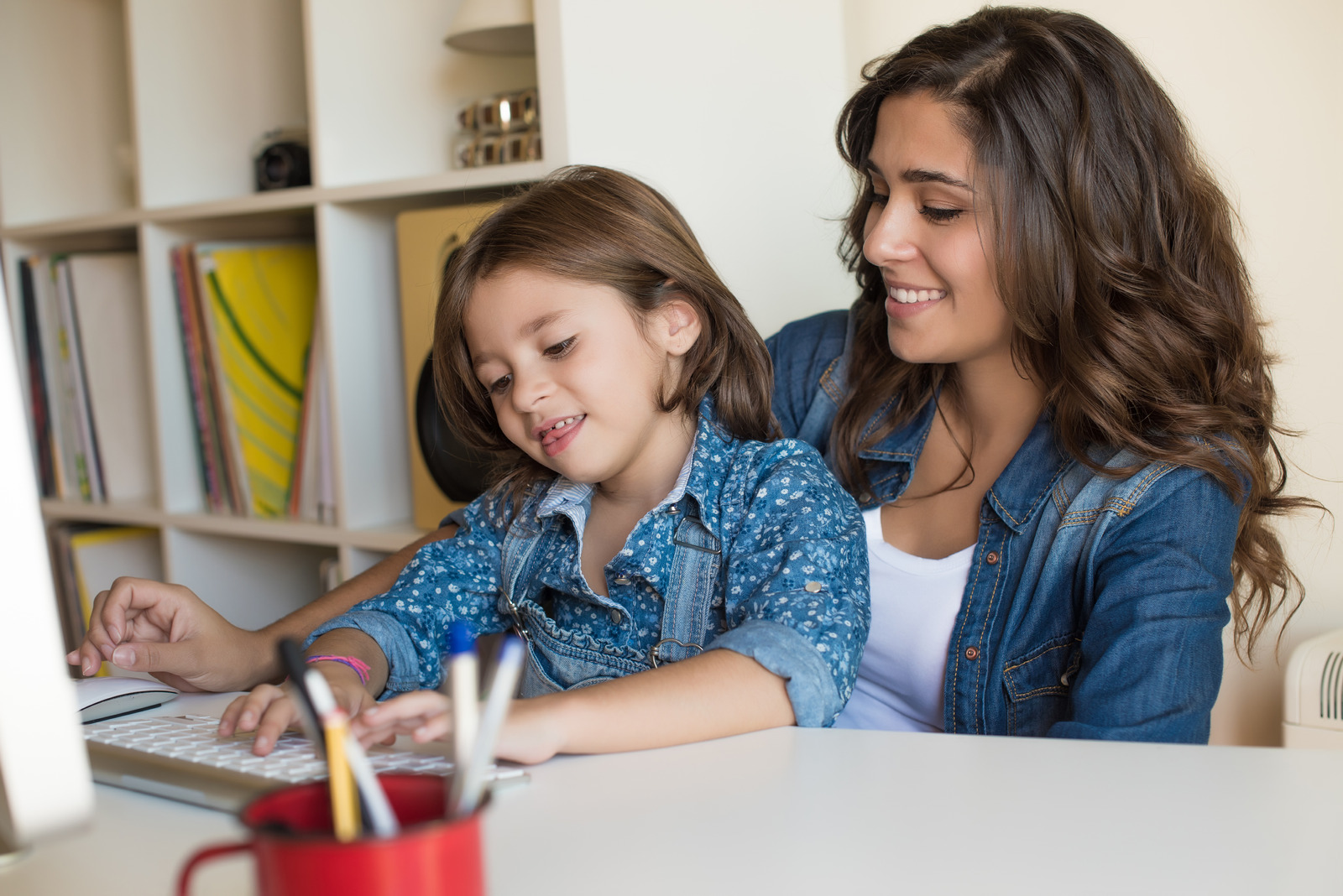 alt="Young woman with little girl using computer at home, self isolating"