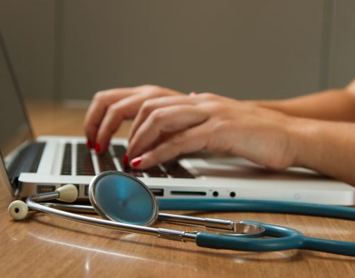 person sitting while using laptop computer and green stethoscope near