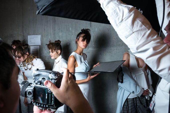 person holding camera taking photo of woman standing near gray wall