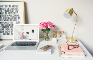 MacBook Air beside gold-colored study lamp and spiral books