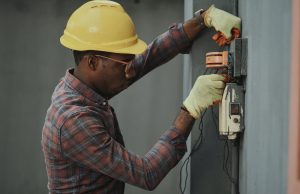 man in brown and white plaid dress shirt and yellow hard hat holding black and orange