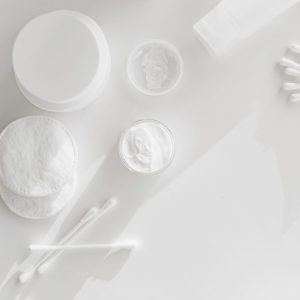 Cotton pads, cotton buds and open jars of face cream on a white surface
