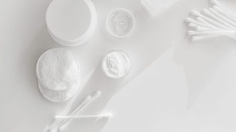Cotton pads, cotton buds and open jars of face cream on a white surface