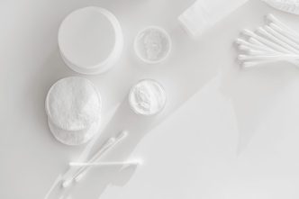 Cotton pads, cotton buds and open jars of face cream on a white surface