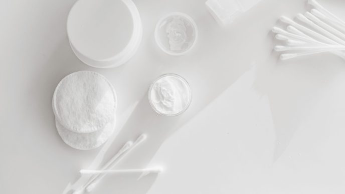 Cotton pads, cotton buds and open jars of face cream on a white surface