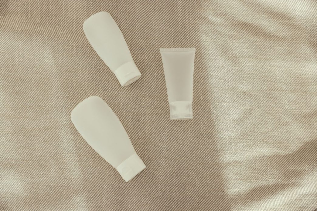 Three plain white skincare tubes laid on a linen cloth
