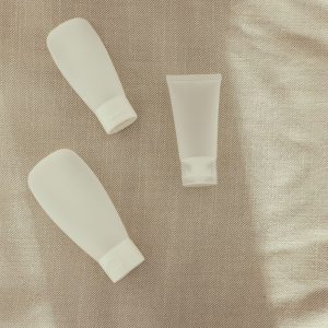 Three plain white skincare tubes laid on a linen cloth