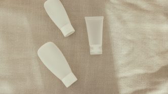 Three plain white skincare tubes laid on a linen cloth