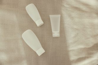 Three plain white skincare tubes laid on a linen cloth
