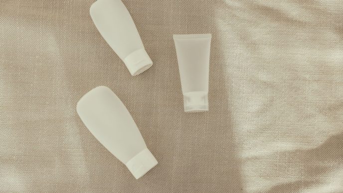 Three plain white skincare tubes laid on a linen cloth