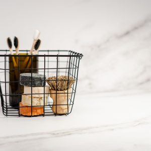 Wire basket holding bars of soap, bamboo toothbrushes and a wooden brush on a white marble surface