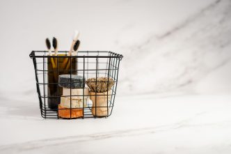Wire basket holding bars of soap, bamboo toothbrushes and a wooden brush on a white marble surface