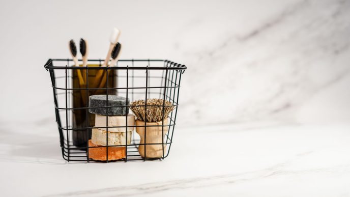 Wire basket holding bars of soap, bamboo toothbrushes and a wooden brush on a white marble surface