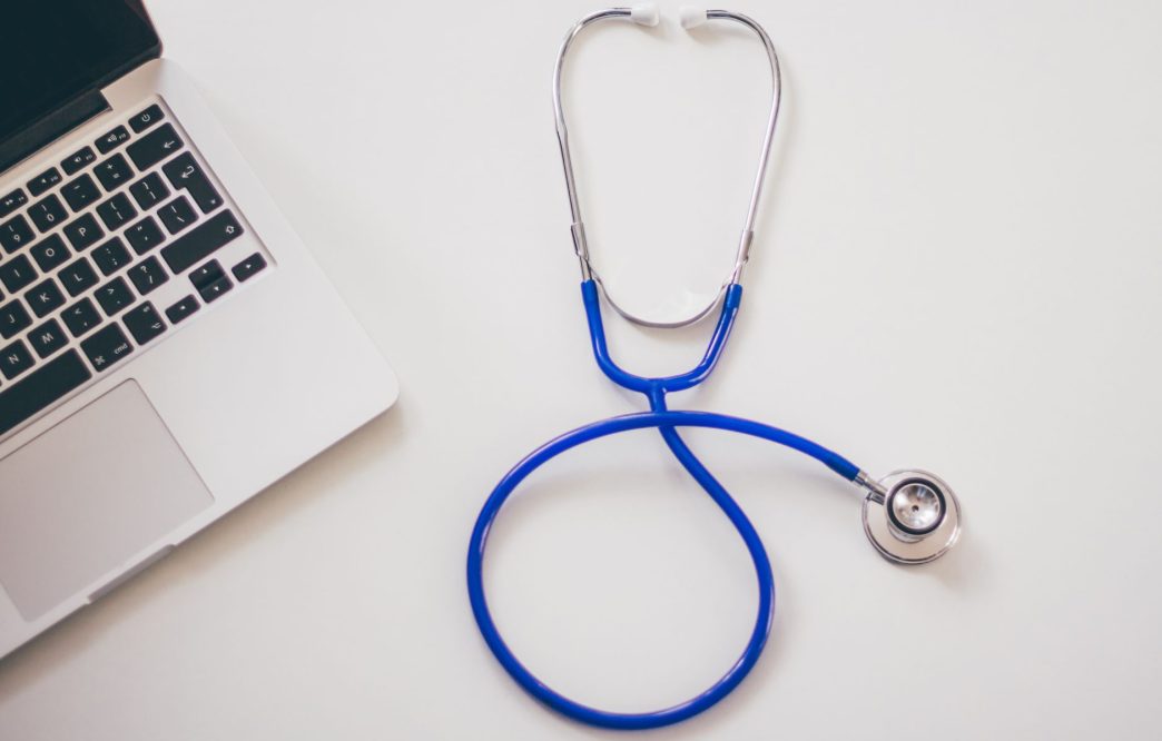 Blue stethoscope beside a laptop on a white desk