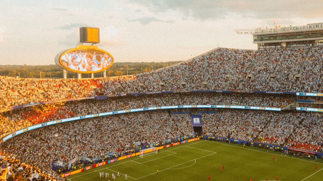 A packed football stadium at sunset during a match