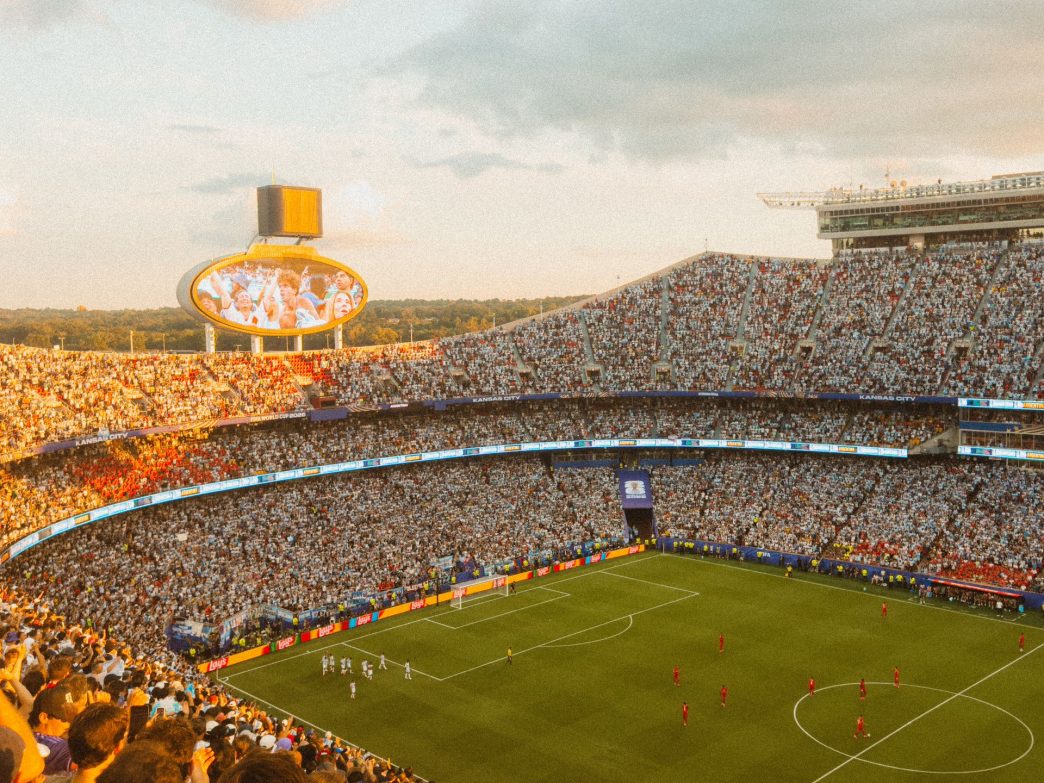 A packed football stadium at sunset during a match